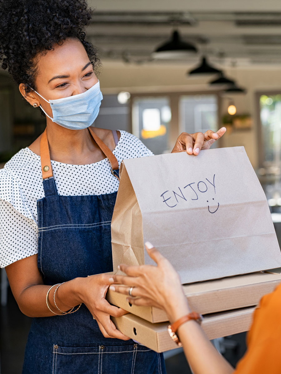 A picture of a waitress handing a to-go order bag to a customer.