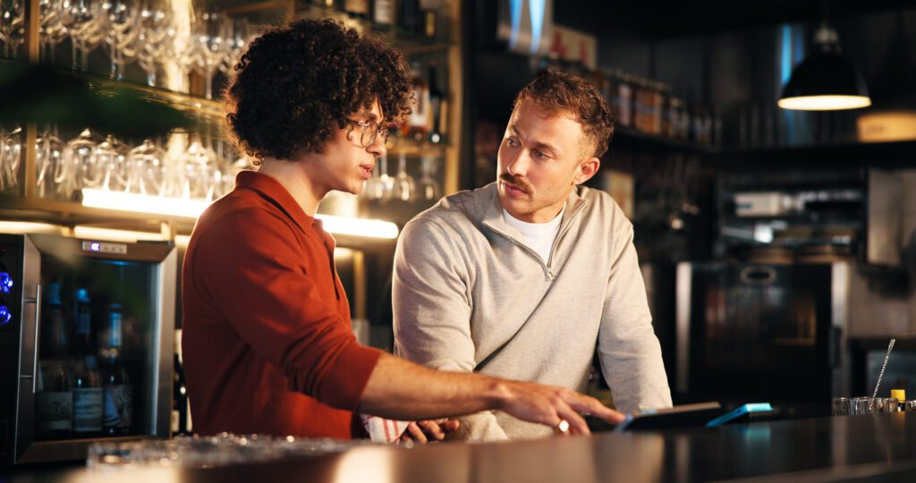 Bar, manager and training with tech for order, teamwork and explaining system to employee and night. Pub, server and people with app to process transactions, working late or help with sales data